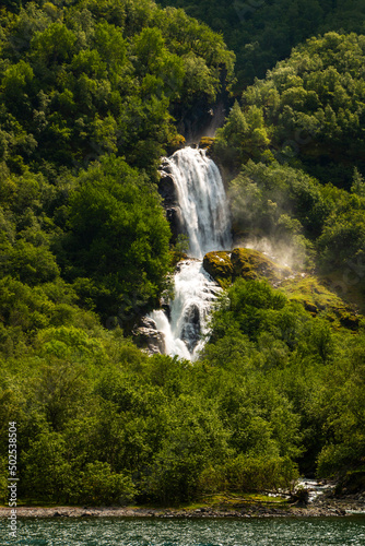 Beautiful waterfall between green trees on Nærøyfjord in early summer in Norway