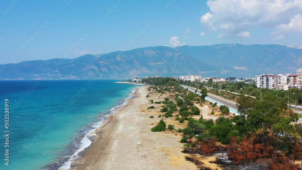 aerial drone panning low across a highway towards a white sandy tropical beach with the Mediterranean Sea and a coastal beach town in Finike Turkey on a sunny summer day aerial drone panning low across a highway towards a white sandy tropical beach with the Mediterranean Sea and a coastal beach town in Finike Turkey on a sunny summer day