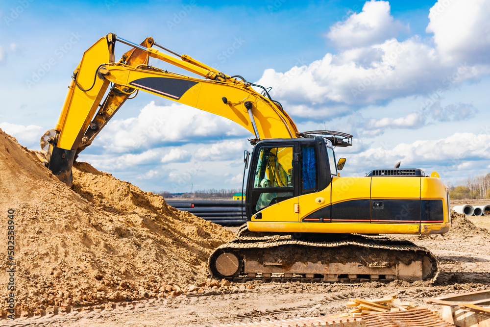 Two powerful excavators work at the same time on a construction site, sunny blue sky in the background. Construction equipment for earthworks. Two powerful excavators work at the same time on a construction site, sunny blue sky in the background. Construction equipment for earthworks.