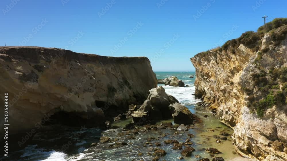 Tidal seawater between two cliffs with waves rolling in along the Pacific coast - aerial push in flyover in slow motion Tidal seawater between two cliffs with waves rolling in along the Pacific coast - aerial push in flyover in slow motion