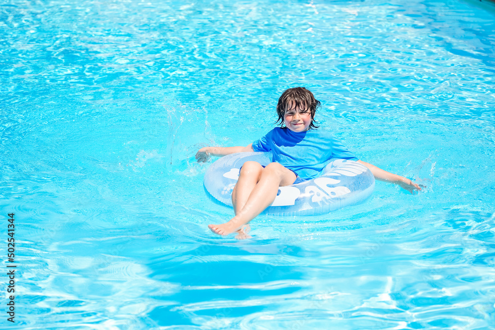 Boy relaxing on an inflatable swim ring in a sunny day, spending time in a swimming pool, aquapark resort hotel. Summer holidays concept.