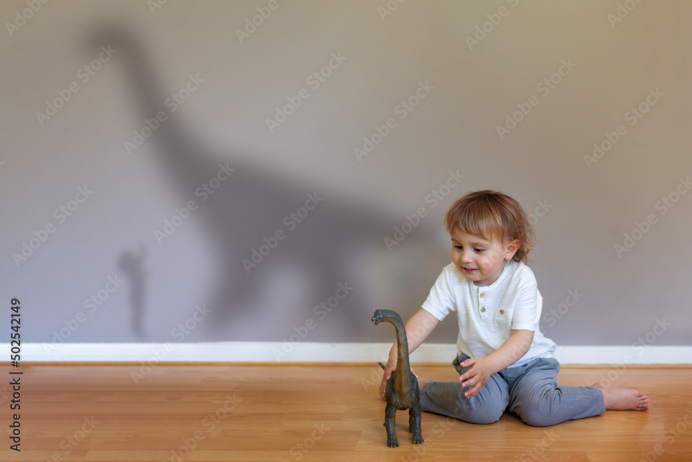 Naklejka premium Preschool boy playing with dinosaur toy indoor. Child's imagination concept. Shadow on the wall. 