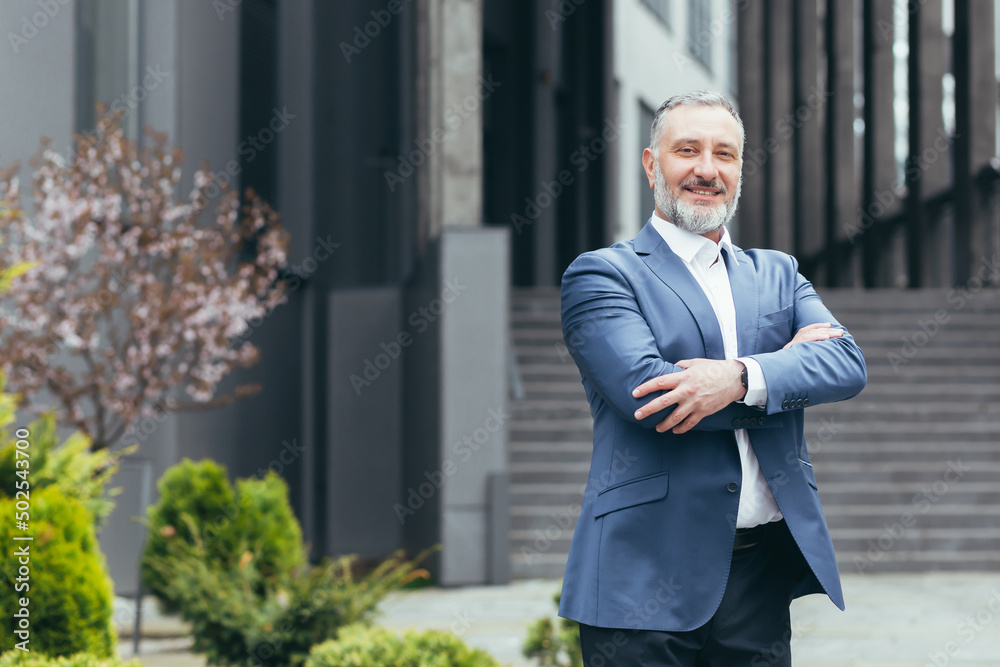 Successful boss business leader man looking at camera with arms crossed and smiling, gray-haired businessman in business suit Successful boss business leader man looking at camera with arms crossed and smiling, gray-haired businessman in business suit