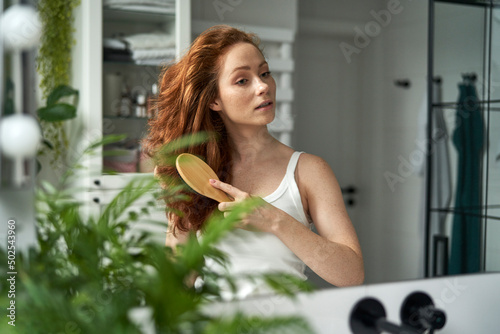 Bilde på lerret Redhead woman brushing hair in the bathroom
