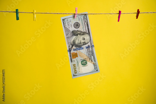 The $100 bill hangs on a yellow background.