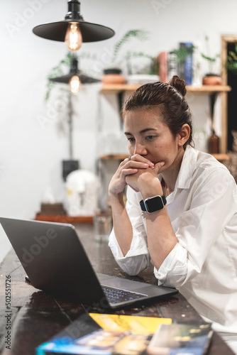 Asian woman stressing working on laptop from home, vertical image.