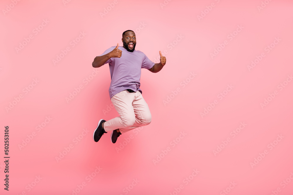 Photo of excited pretty guy wear purple t-shirt jumping high thumbs up empty space isolated pink color background