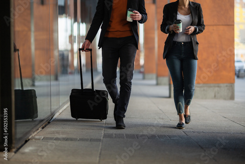 Business man and woman walking and drinking coffee. Businesspeople traveling together with luggage. © Nikola Spasenoski