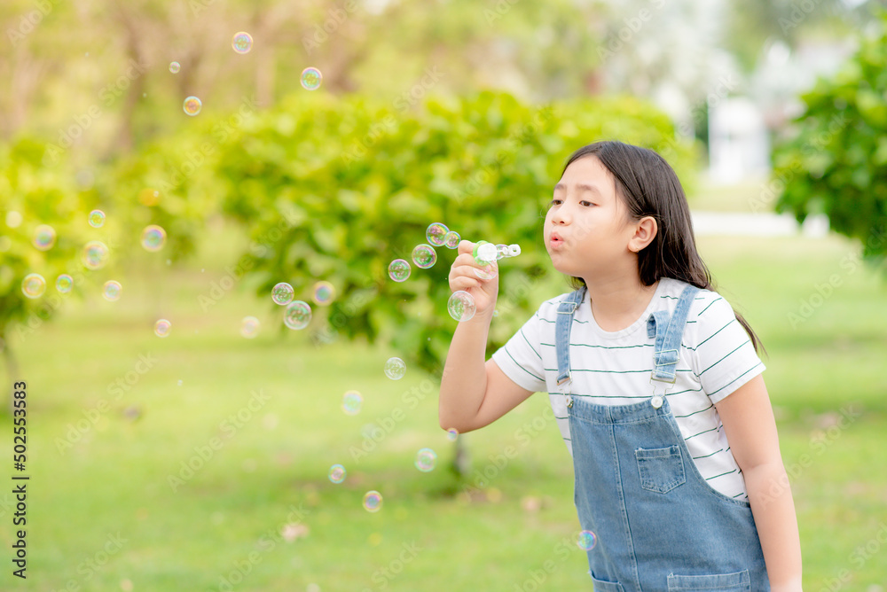 A cute girl is having fun blowing bubbles in the middle of a meadow and green trees.