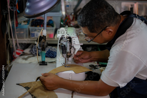 Sewing process of the leather belt. Man's hands behind sewing. Leather workshop.