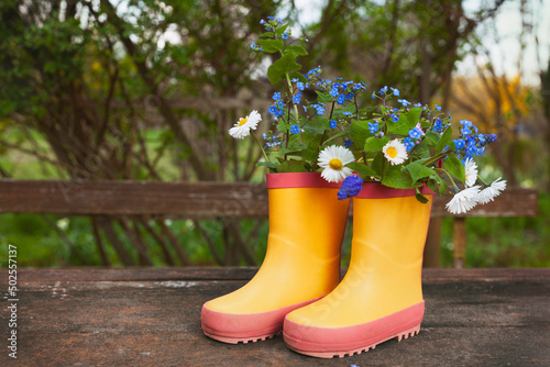 Yellow rubber boots with spring flowers bouquet on rough rural wooden background. Natural background
