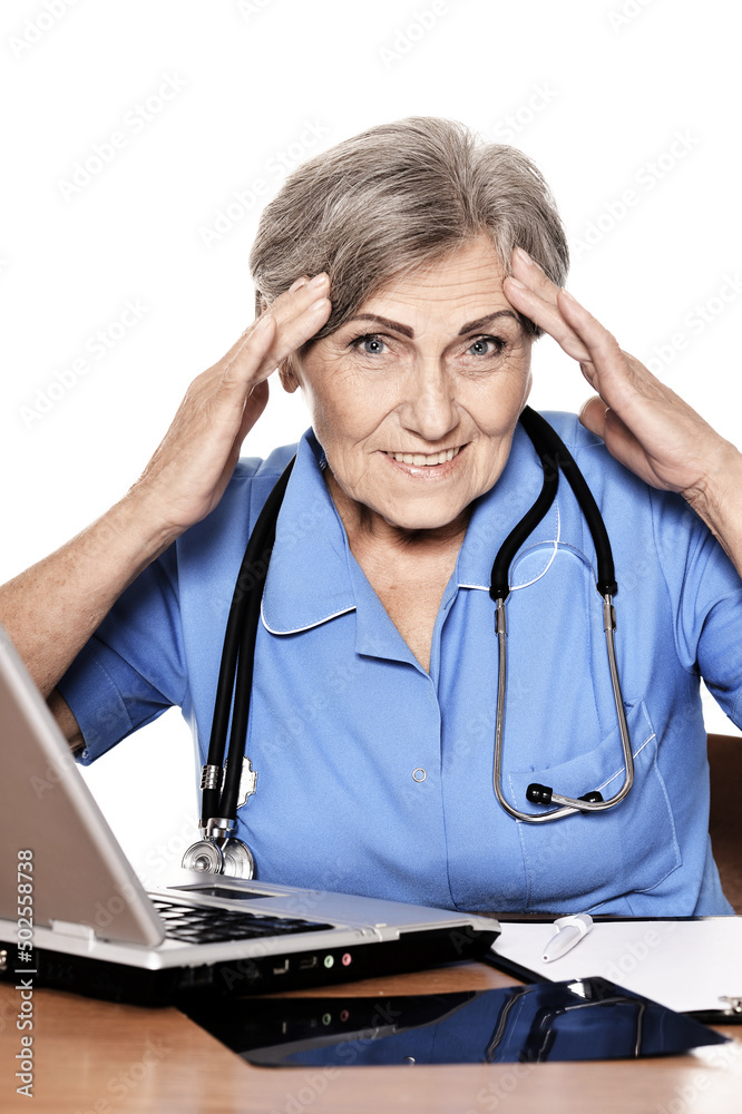 Serious elderly woman doctor sitting at table with computer Serious elderly woman doctor sitting at table with computer Serious elderly woman doctor sitting at table with computer Serious elderly woman doctor sitting at table with computer