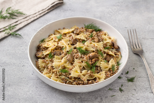Traditional Jewish dish kasha varnishkes: buckwheat, pasta, champignon mushrooms, fried onions with herbs on a gray textured background, vegan food photo