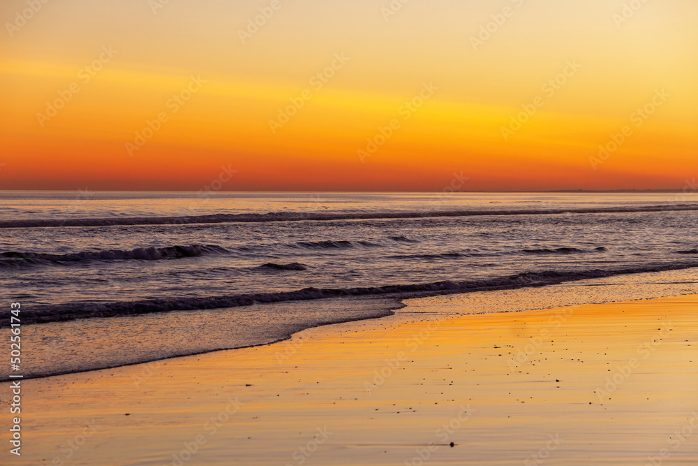 
Sunset on beach with reflections of the orange sky in the water