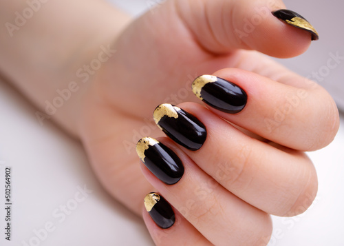 Beautiful hand of a young woman with manicure, black gel polish with gold foil