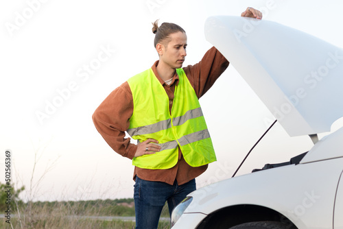 Thoughtful young man looking at the engine of his car so he can repair it and get home before it gets dark