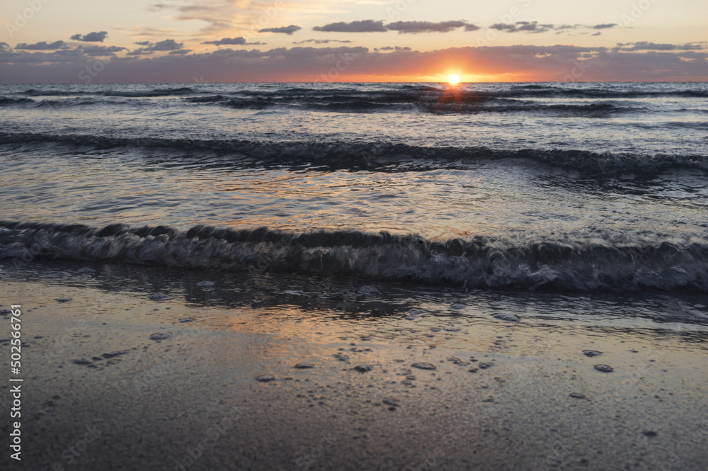 Tramonto sul mare con onde e riflesso del sole sull'acqua e sulla sabbia.