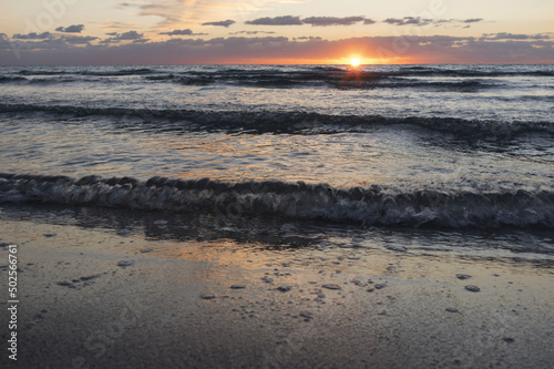 Tramonto sul mare con onde e riflesso del sole sull'acqua e sulla sabbia.