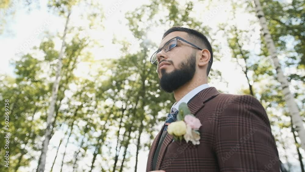 Brutal Caucasian man with a beard in glasses and a stylish brown suit walks in the park adjusting his tie and considering a business plan Brutal Caucasian man with a beard in glasses and a stylish brown suit walks in the park adjusting his tie and considering a business plan