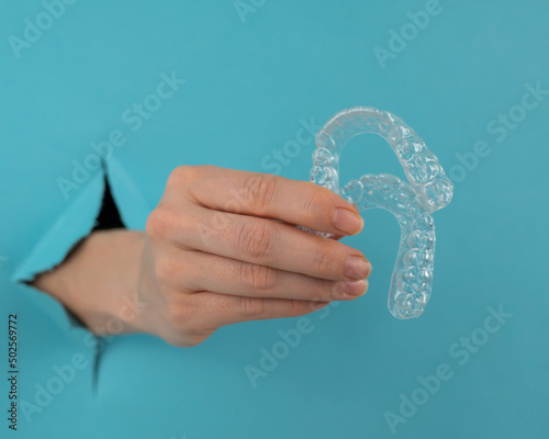 A female hand sticking out of a hole from a blue background holds removable night retainers. 