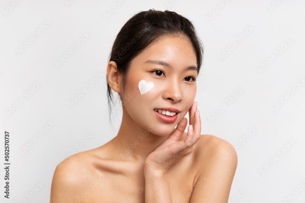 Asian woman posing with heart shaped cream on cheek Asian woman posing with heart shaped cream on cheek