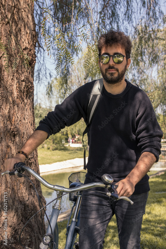 Obraz premium Young man with curly hair wearing sunglasses and backpack enjoying a sunny day with his bike.