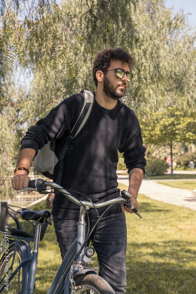 Young man with curly hair wearing sunglasses and backpack enjoying a sunny day with his bike. Young man with curly hair wearing sunglasses and backpack enjoying a sunny day with his bike.