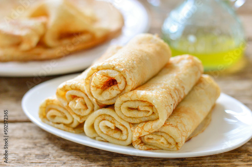 Thin pancakes (bliny). Pancakes rolled into tubes on a white plate. Wooden background.