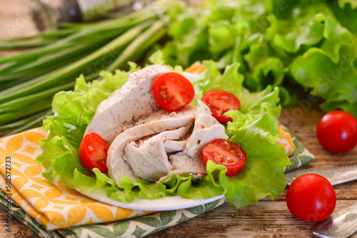 Boiled chicken fillet garnished with lettuce and cherry tomatoes. Wooden background.