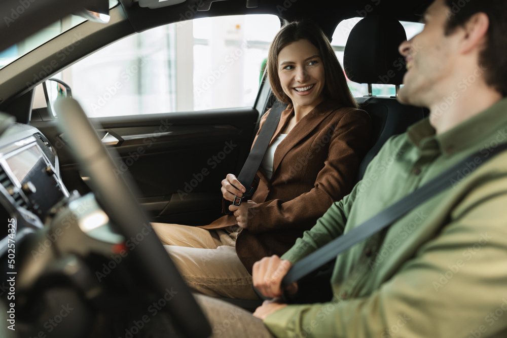 Happy young couple sitting in automobile salon, satisfied with test drive, discussing purchase of new car at auto dealership