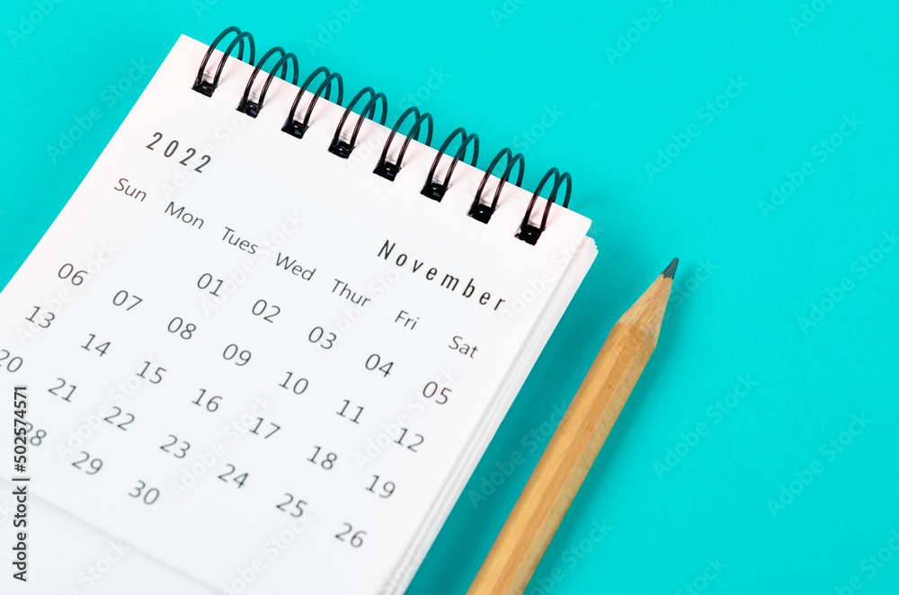 November 2022 desk calendar with wooden pencil on light blue background.