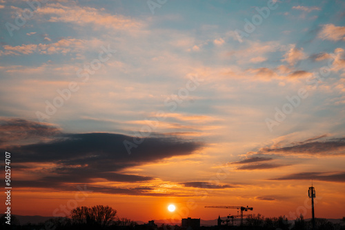 Dramatic sunset sky with orange clouds and tree silhouette. Screen and photo background