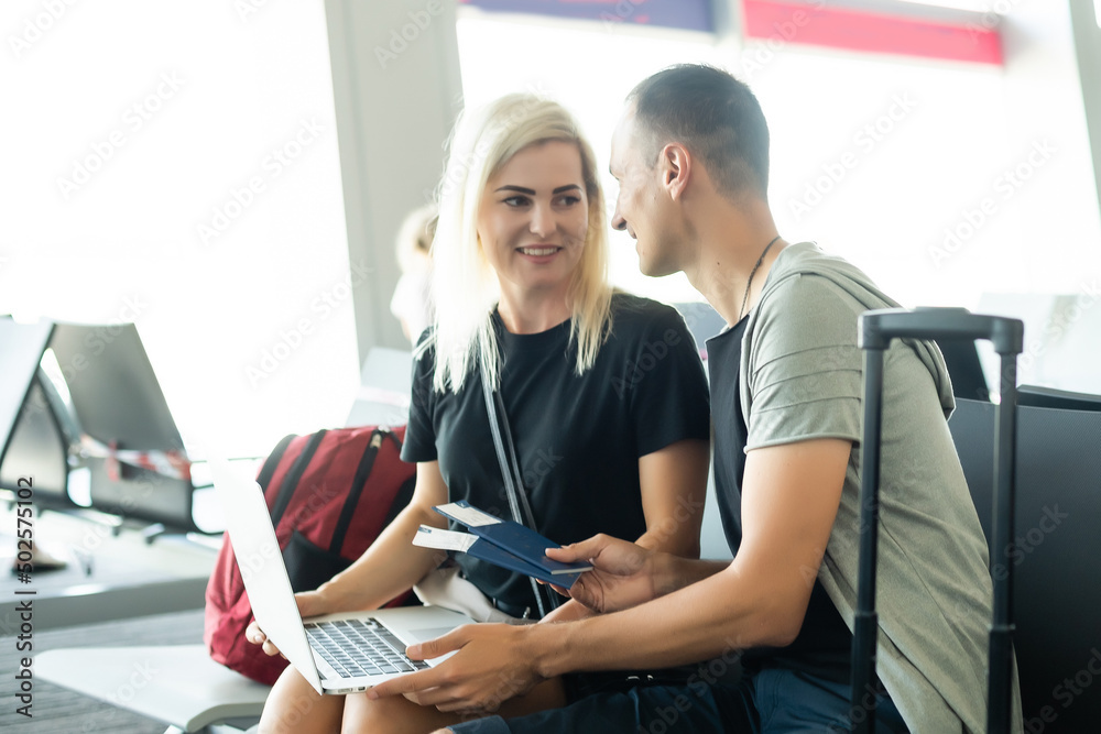 © Angelov - couple sitting with laptop, phone and suitcase at the waiting hall in the airport. Business travel concept