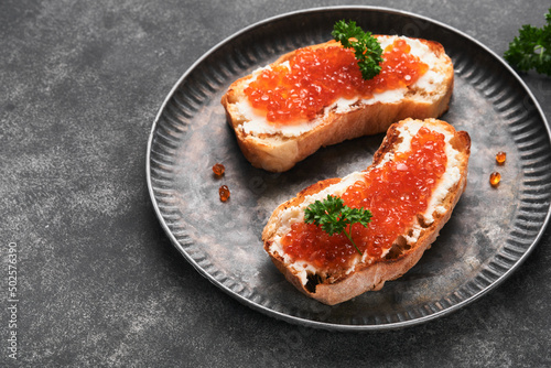 Two dandwiches with red caviar. Salmon red caviar in bowl and sandwiches server on old iron plate on old black table background. Top view. Copy space.