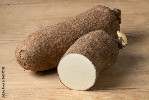  Whole and halved raw African yam on wooden background close up