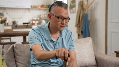 closeup portrait of old male asian dementia patient sitting alone with a stick and blank expression on face in the living room at home