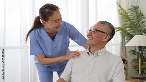 Closeup of caring Asian woman nursing aide talking and encouraging older male patient during home visit. Domiciliary care for elderly senior concept