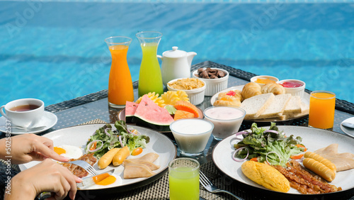 Vacation breakfast table. Woman hands cutting sunny side eggs at luxury restaurant or villa hotel room near the blue swimming pool on tropical holidays. Breakfast for two, romantic, honeymoon travel. © TravelMedia