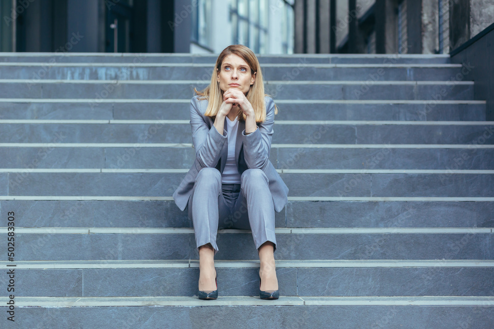Depressed sad woman sitting on the stairs of a business building, businesswoman in business clothes tired Depressed sad woman sitting on the stairs of a business building, businesswoman in business clothes tired