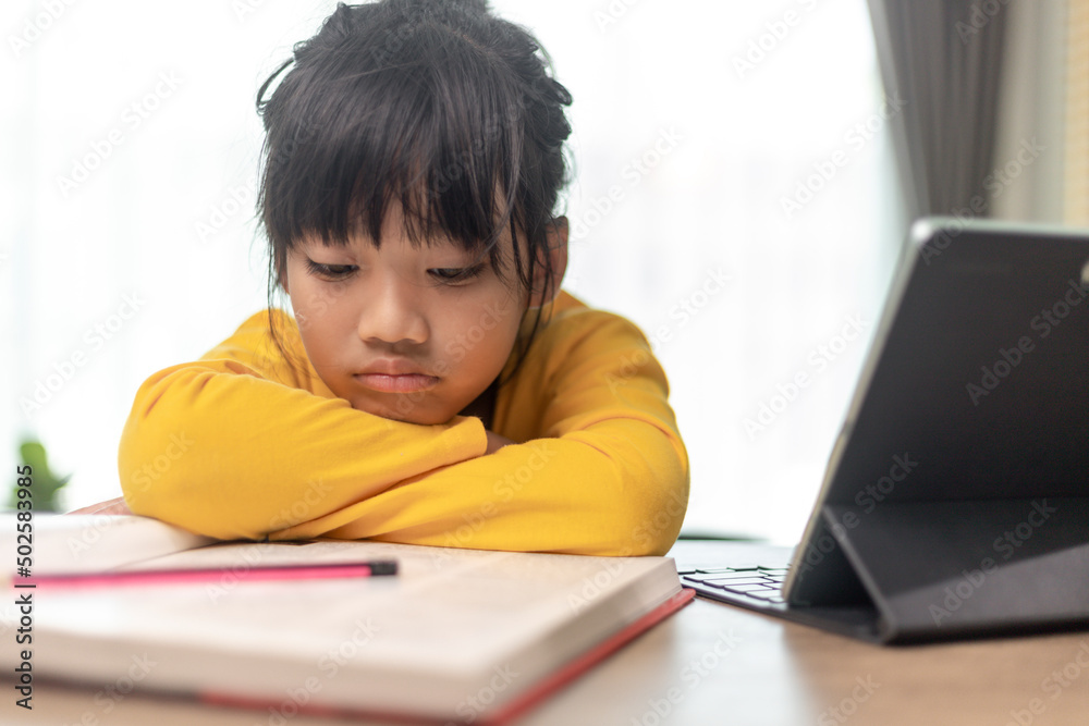 Little Asian girl sitting alone and looking out with a bored face, Preschool child laying head down on the table with sad bored with homework, spoiled child Little Asian girl sitting alone and looking out with a bored face, Preschool child laying head down on the table with sad bored with homework, spoiled child