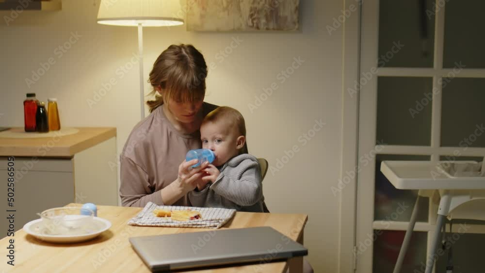 Baby boy drinking water from bottle and eating puff pastry while sitting with loving mother at kitchen table Baby boy drinking water from bottle and eating puff pastry while sitting with loving mother at kitchen table