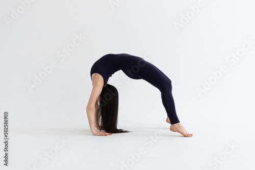 a beautiful young girl with dark hair stands in the Urdhva Dhanurasana pose on a white background. Yoga class