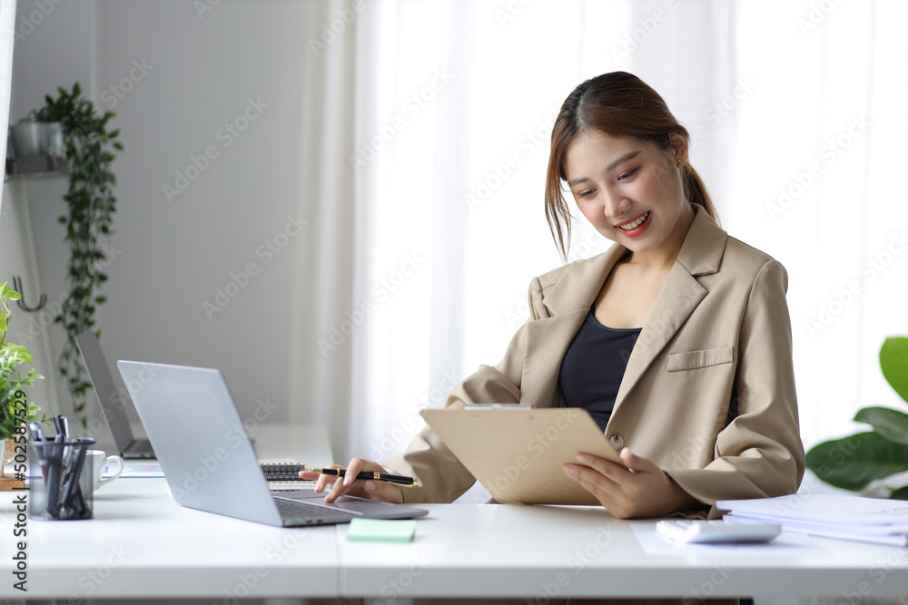 Attractive Asian businesswoman in casual office working on laptop and reading documents. Attractive Asian businesswoman in casual office working on laptop and reading documents.