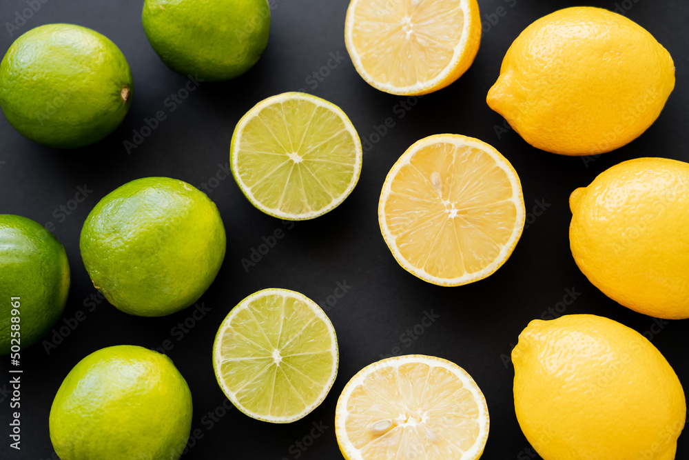 Flat lay of whole and cut lemons and limes on black background