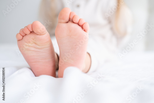 Close up kid child barefooted legs feet lying on white bed linen. Neutral pastel light color tones