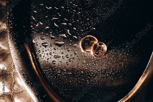 Macro photography wedding rings in water drops, engagement rings symbolizing love, with gold shades.