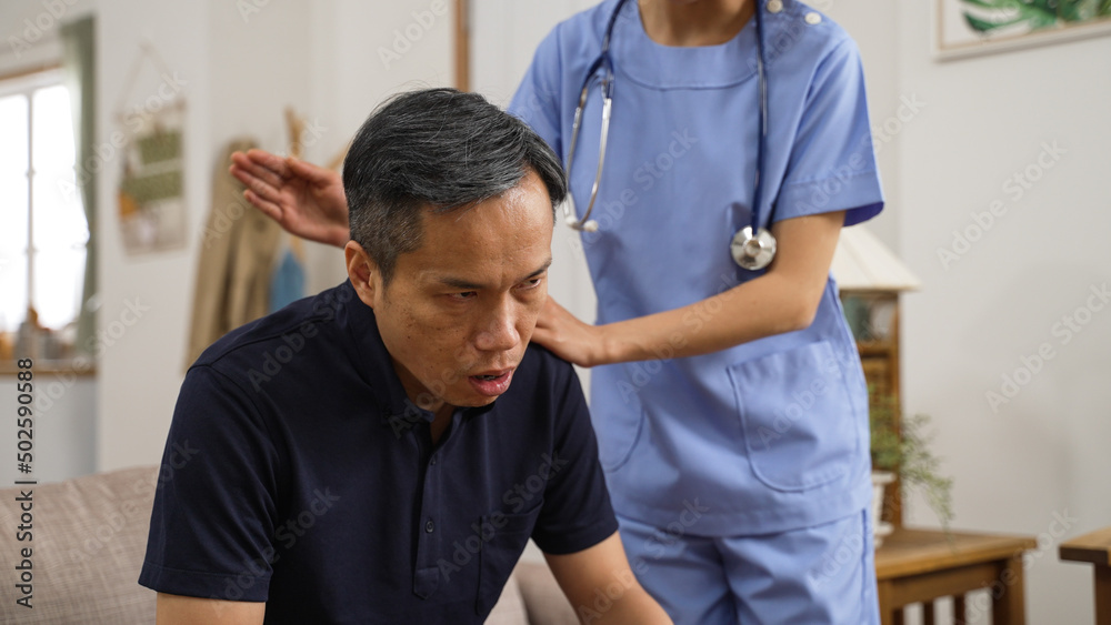 asian female nurse tapping mature patient’s back to help clear the mucus as the Japanese man is coughing on sofa at home. social care assistance concept asian female nurse tapping mature patient’s back to help clear the mucus as the Japanese man is coughing on sofa at home. social care assistance concept