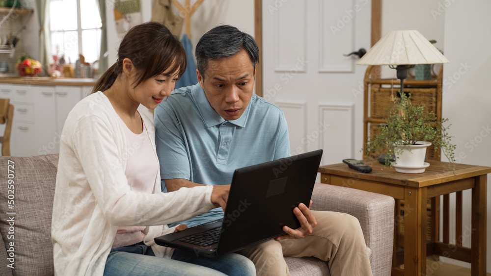portrait of asian grandfather learning how to use laptop computer with adult granddaughter’s help in the living room at home. they point and look at the monitor while talking portrait of asian grandfather learning how to use laptop computer with adult granddaughter’s help in the living room at home. they point and look at the monitor while talking