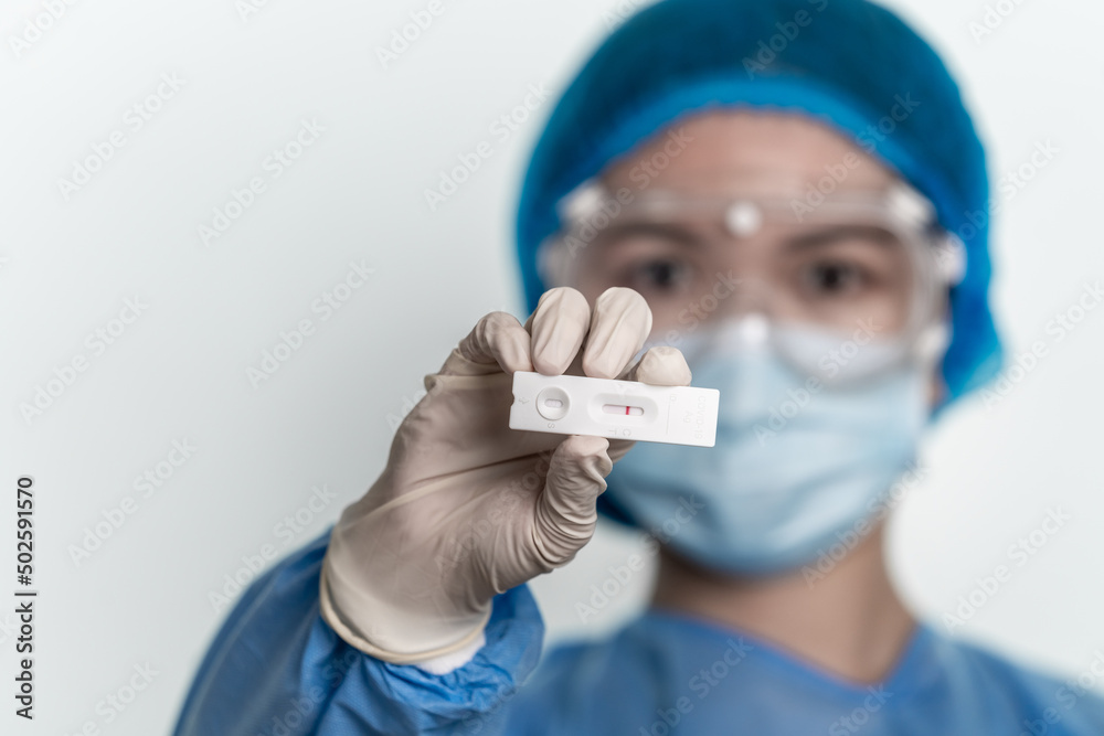 Doctor wearing protective suit is holding covid-19 self test kits, showing negative results. 