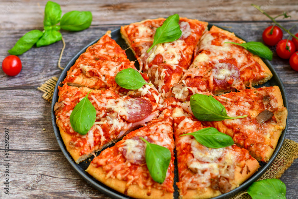 Close up of classic Italian Pizza with Ham and salami . Fresh basil,tomato sauce ,mozzarella cheese , mushrooms and green peppers Close up of classic Italian Pizza with Ham and salami . Fresh basil,tomato sauce ,mozzarella cheese , mushrooms and green peppers